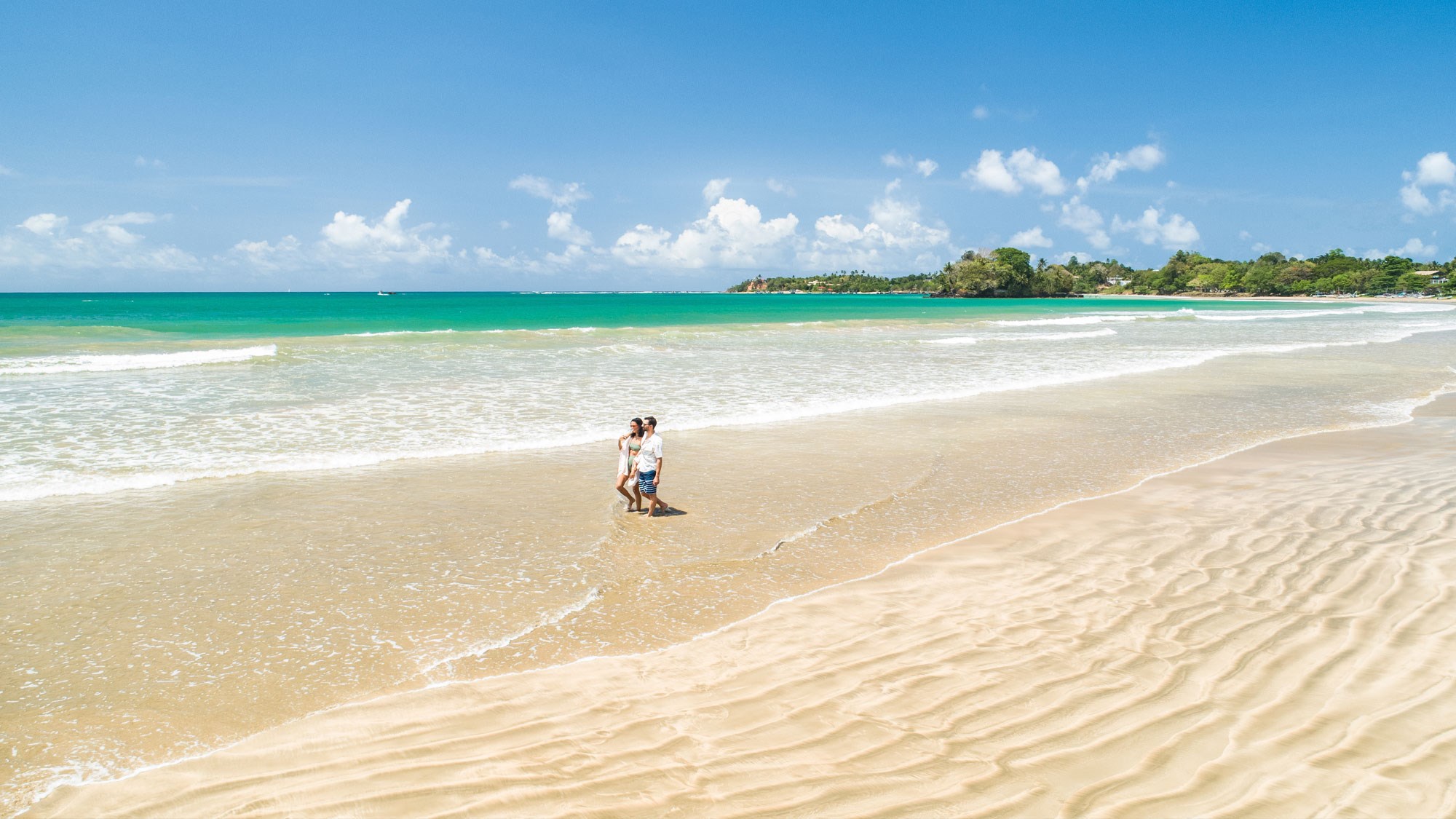 Couple walking across golden sand in Weligama