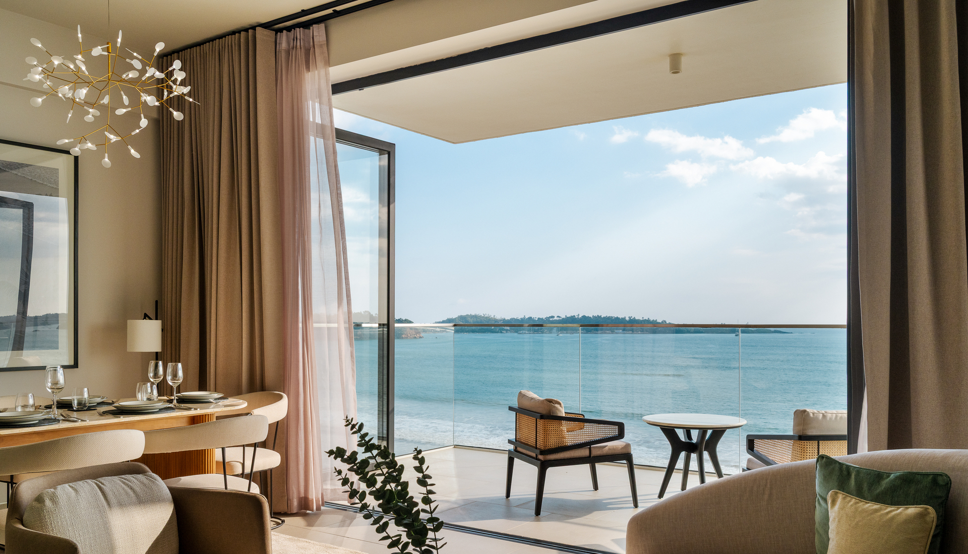 A Beach View One Bed: the living and dining room, open to a balcony with chairs and a table above the beach and Weligama Bay